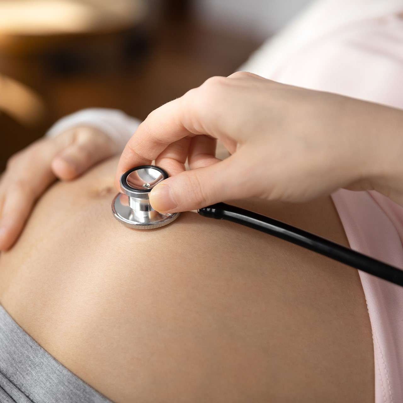 OBGYN doctor using stethoscope on pregnant woman stomach to listen to heartbeat of baby